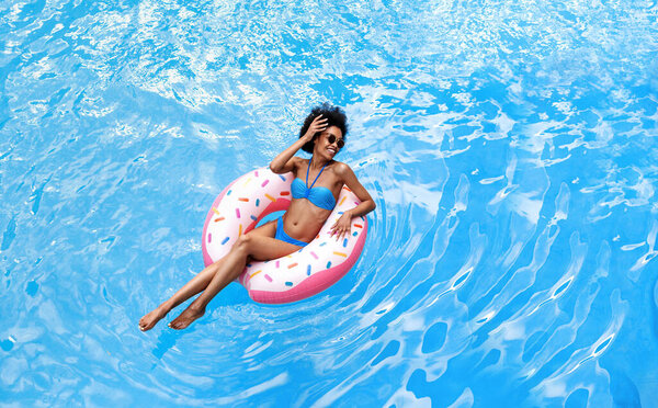 Афроамериканка в бикини, плавающая на надувном кольце в бассейне, копировальная площадка
