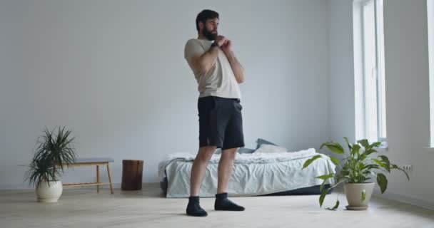 Młody brodaty mężczyzna obracający biodrami, ćwiczący w domu — Wideo stockowe