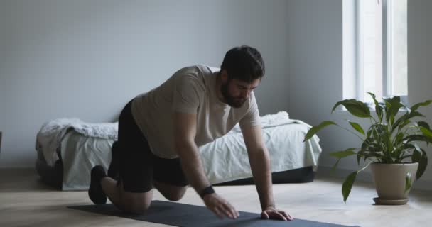 Młody mężczyzna rozciągający się na macie fitness w domu — Wideo stockowe