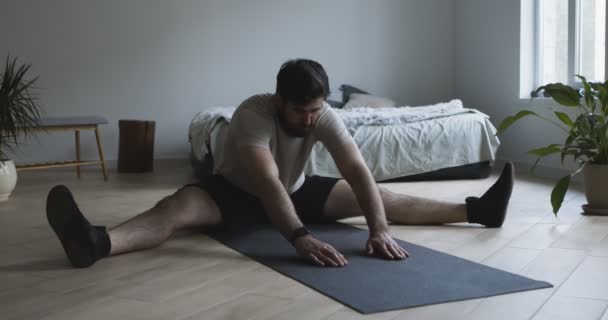 Junger Mann streckt Beine, trainiert zu Hause auf dem Boden — Stockvideo