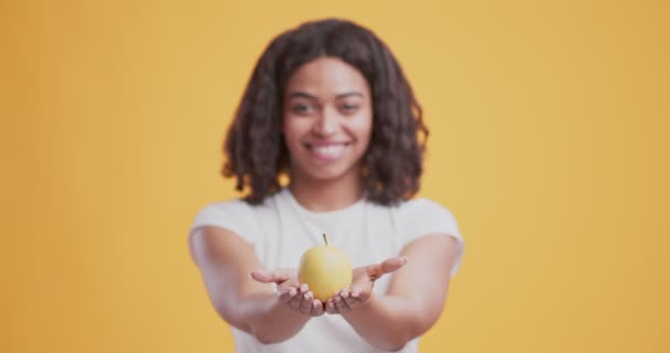 Χαμογελώντας αφροαμερικανή κοπέλα που προσφέρει φρέσκο μήλο στην κάμερα — Αρχείο Βίντεο