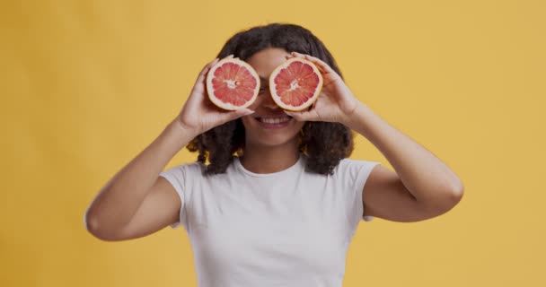 Весела афро-американська дівчина танцює з грейпфрутовими скибками біля очей. — стокове відео