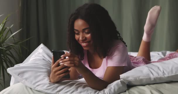 Milenyum Afrikalı Amerikalı kadın yatakta cep telefonuyla geziniyor. — Stok video
