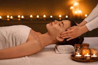 Rahatlamış genç bir kadın romantik spa atmosferinde kafa masajı yaptırıyor.