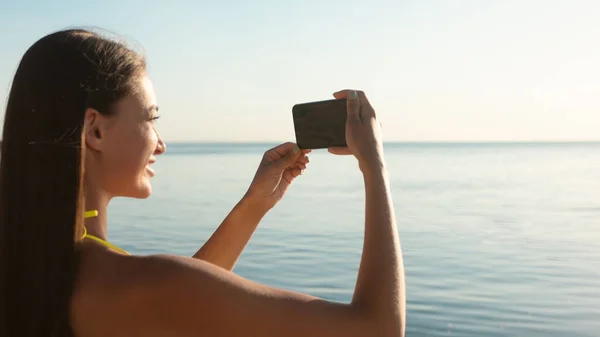 Menina com Smartphone tirar fotos do mar ao ar livre, vestindo roupa de banho — Fotografia de Stock