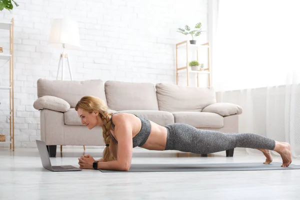 Sport und Arbeit online. Frau in Sportbekleidung macht Planke und blickt auf Laptop am Boden — Stockfoto