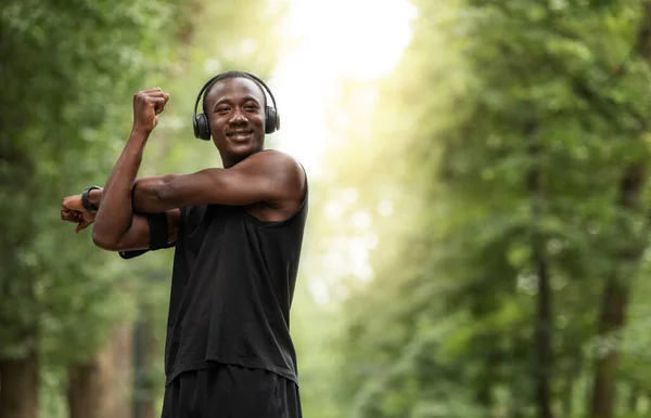 Alegre deportista africano haciendo ejercicio en el parque, estirando los brazos —  Fotos de Stock