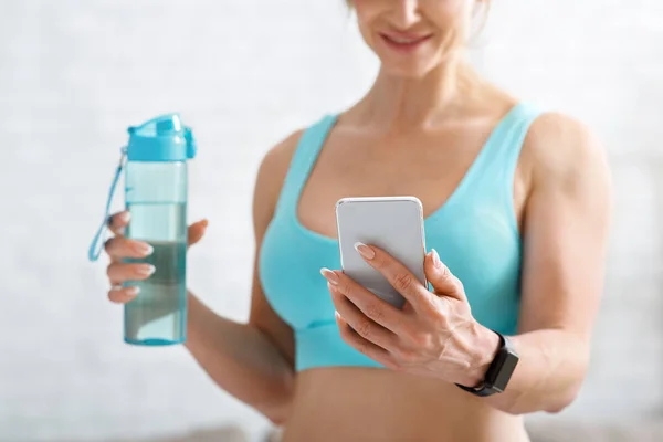 Boas notícias no smartphone. Mulher muscular com garrafa de água olha para o telefone — Fotografia de Stock