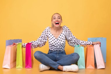 Stüdyoda alışveriş torbalarıyla oturan aşırı mutlu bir kadın.