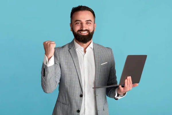 Happy corporate executive with laptop gesturing YES in victory over blue background — Stok Foto