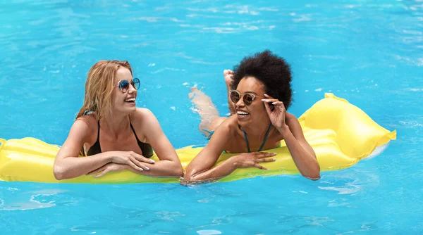 一緒に夏の楽しみ。Best girl friends floating on lilo and laughing at outdoor swimming pool — ストック写真
