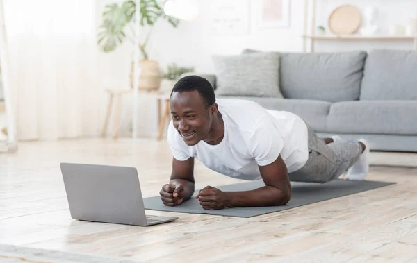 Jovem negro exercitando em casa, usando laptop — Fotografia de Stock