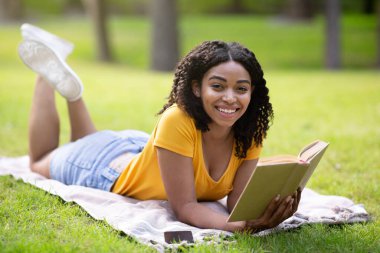Parkta piknik battaniyesine uzanmış ilginç kitaplar okuyan neşeli siyah kız.