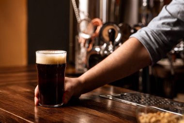 Barda köpüklü taze koyu bira. Barmen tezgahta köpüklü koyu bir içeceğe bardak verir.