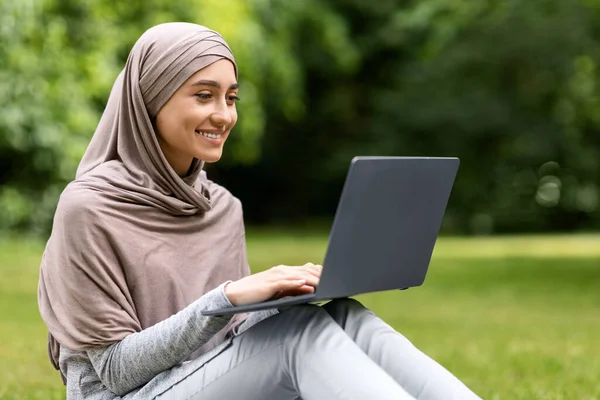 Sonriendo chica bastante musulmana usando el ordenador portátil mientras descansa en el parque — Foto de Stock