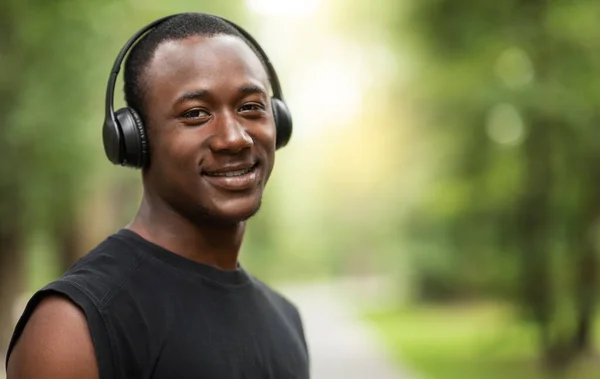 Retrato de chico negro sonriente con auriculares inalámbricos, entrenamiento al aire libre —  Fotos de Stock