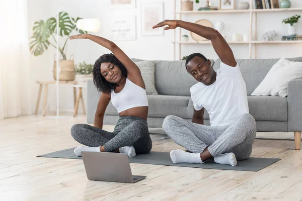 Esportivo casal africano alongamento em casa, assistindo aula on-line — Fotografia de Stock