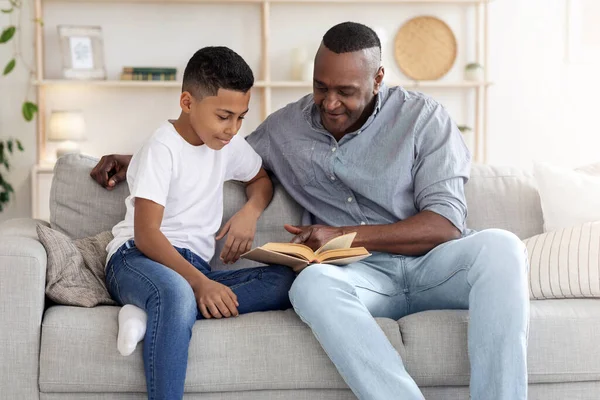 Pastime With Grandpa. Senior African Man Reading Book With Grandson At Home