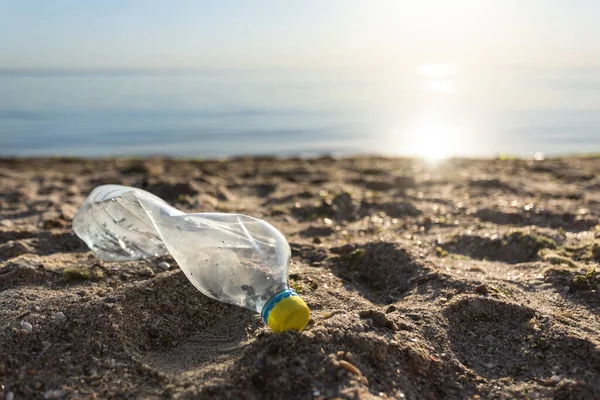 Garrafa de plástico que jaz na praia perto da água, fundo da poluição do mar — Fotografia de Stock