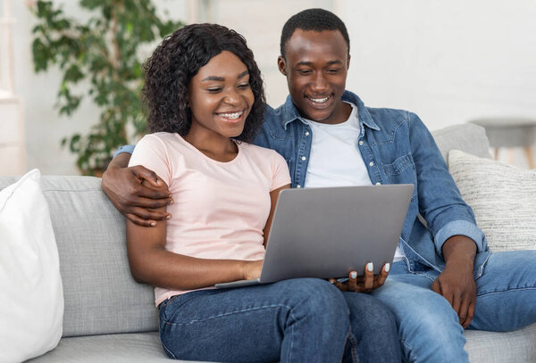 Веселая чернокожая пара использует ноутбук в гостиной дома
