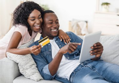 Mutlu evli Afrikalı çift dijital tablet kullanarak internetten bir şeyler alıyor.