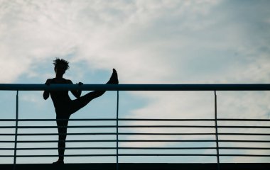 Afrikalı Amerikalı bir kızın silueti gökyüzü arka planında bacaklarını esnetiyor.