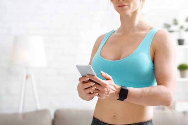 Treinador de fitness remotamente em casa. Mulher muscular com relógio inteligente olha para o telefone — Fotografia de Stock