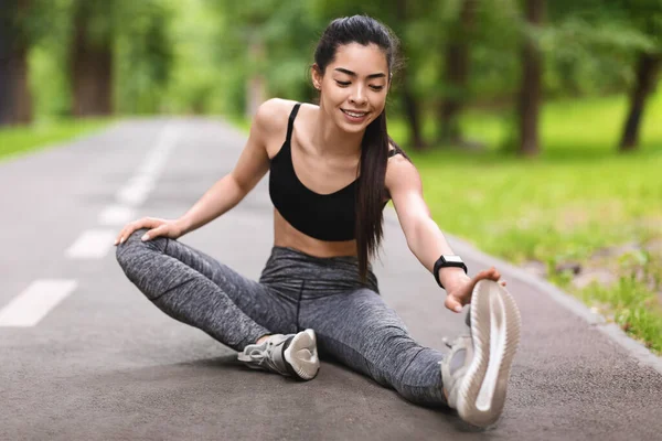 Asiática chica estiramiento de la pierna músculos después de correr en parque, sentado en el camino — Foto de Stock