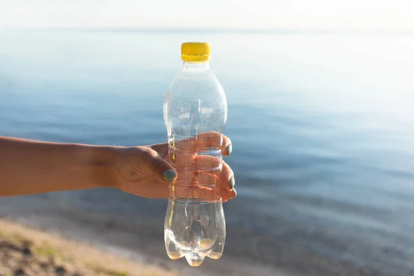 Mão feminina segurando garrafa de plástico usado na praia ao ar livre, cortado — Fotografia de Stock
