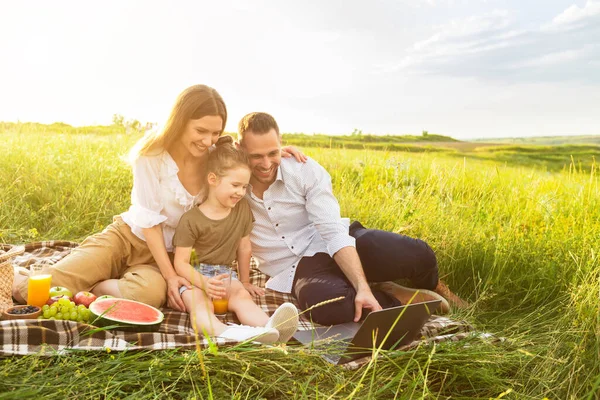 Família feliz em conjunto em um piquenique com laptop — Fotografia de Stock