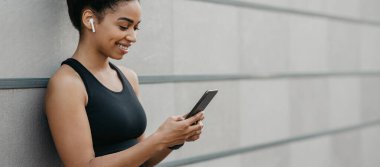 Koşmak için eğitime ve müziğe başlayın. Kablosuz kulaklıklı Afrikalı Amerikalı kız akıllı telefondan bakıyor.