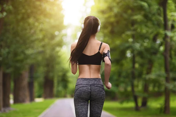 Вид сзади на молодую женщину, бегущую в зеленом городском парке — стоковое фото