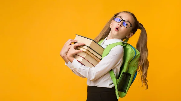 Scuola ragazza oberata di lavoro che tiene libri in piedi su sfondo giallo, Panorama — Foto Stock