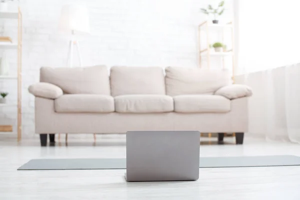 Gym at home. Living room with daylight, sofa, mat on floor and laptop — Stock Photo, Image