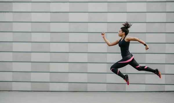 Excelente entrenamiento. chica afroamericana en ropa deportiva se congeló en el aire por encima del suelo, saltando — Foto de Stock