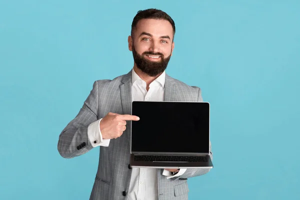 Empreendedor positivo com laptop apontando para a tela vazia com espaço para o seu design sobre fundo azul — Fotografia de Stock