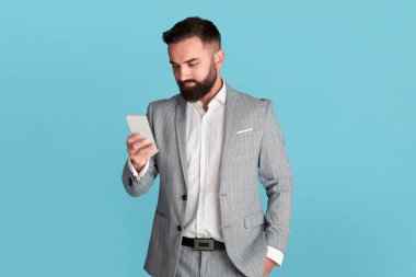 Millennial ofis çalışanı mavi arka planda akıllı telefondan iletişim kuruyor.