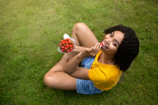 Healthy diet. Above view of fit black girl eating yummy strawberries on green lawn, copy space — Stock Photo, Image