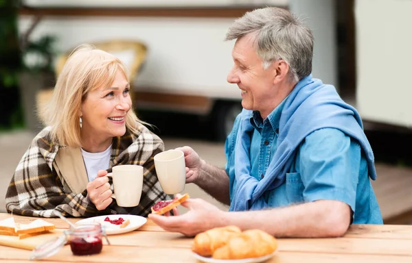 Fröhlich reifer Mann und seine Frau genießen Morgenkaffee mit Marmeladen-Toasts auf dem Zeltplatz — Stockfoto