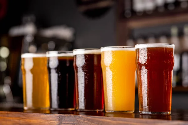 Ambachtelijk bier en industrie. Lager, licht en licht, donker, ongefilterd bier in glazen op houten balie — Stockfoto