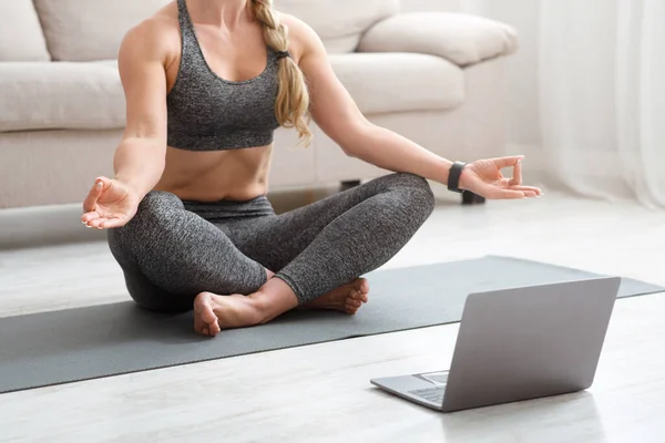 Kobieta w odzieży sportowej siedzi na macie na podłodze z laptopem w pozycji lotosu — Zdjęcie stockowe