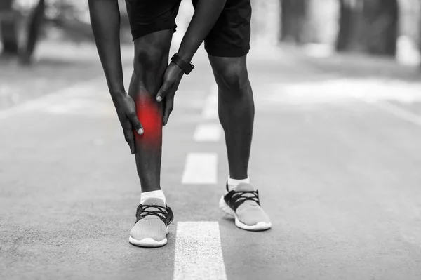 Крупный план африканского спортсмена касающегося травмированной ноги — стоковое фото