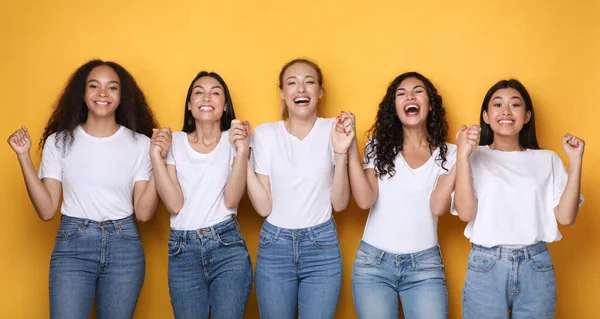 Chicas multiétnicas emocionadas sosteniendo las manos sonriendo a la cámara, fondo amarillo — Foto de Stock