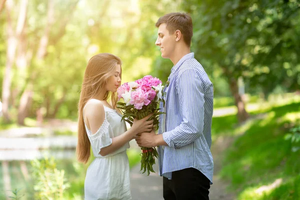 Bella ragazza profumata bouquet di peonie dato dal suo ragazzo al parco — Foto Stock