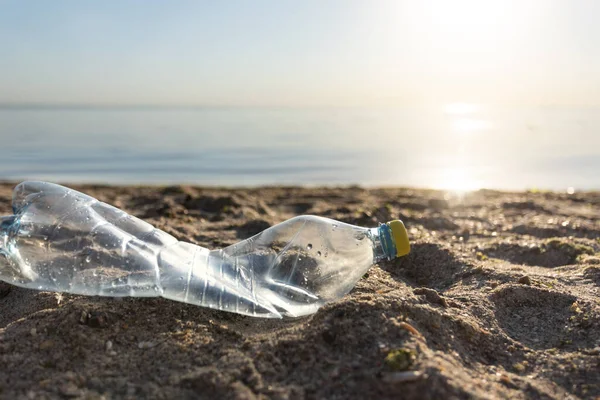 Garrafa de plástico de uso único desperdiçada que jaz no ambiente poluente da praia ao ar livre — Fotografia de Stock