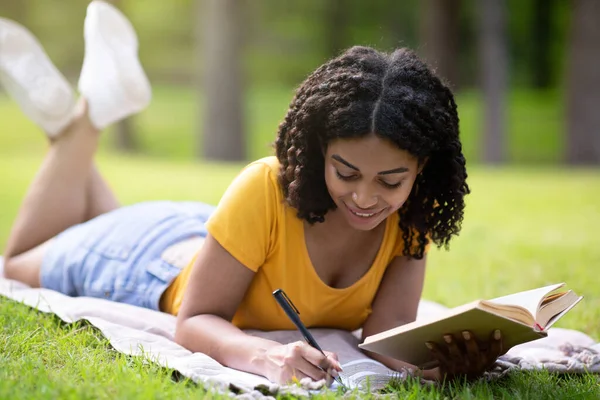 在公园里的野餐毛毯课本上记笔记的黑人女生 — 图库照片