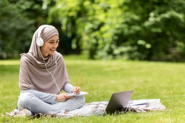 Çalışkan Arap kız parkta internetten ders çalışıyor, laptop kullanıyor.