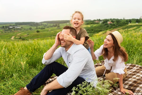 Familia joven feliz jugando adivina quién juego en un picnic — Foto de Stock