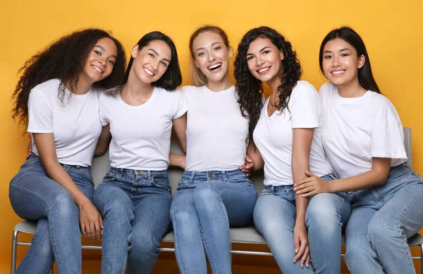 Meninas alegres amigos abraçando sentado no banco em fundo amarelo — Fotografia de Stock