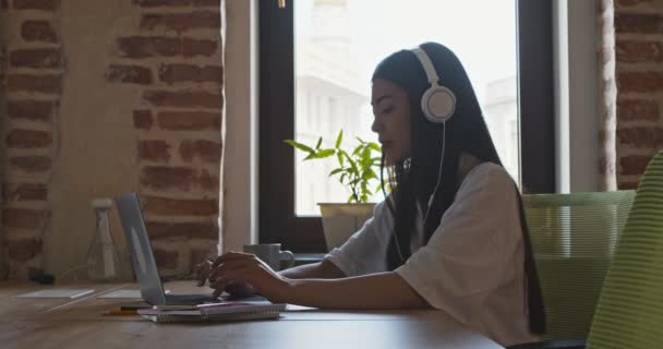 Asiática chica en auriculares escribiendo en el ordenador portátil en la universidad campus — Vídeo de stock